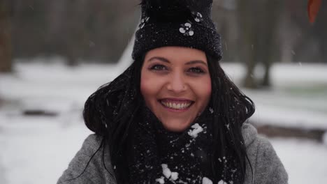 Frau-Im-Winter-In-Einem-Park,-Die-Hände-Hochhält-Und-Schnee-Auf-Sie-Fallen-Lässt,-Während-Sie-Lächelt