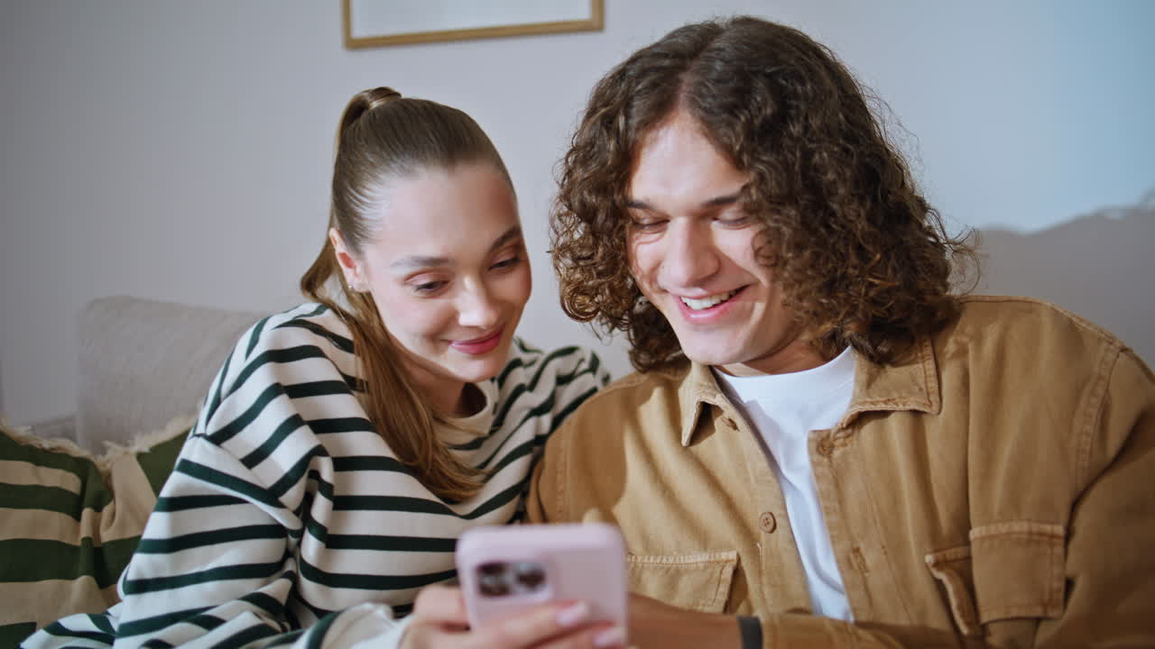 Loving spouses smiling together relaxing on cozy couch with smartphone closeup
