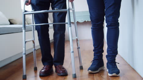 male nurse helping senior man use walking frame, low section