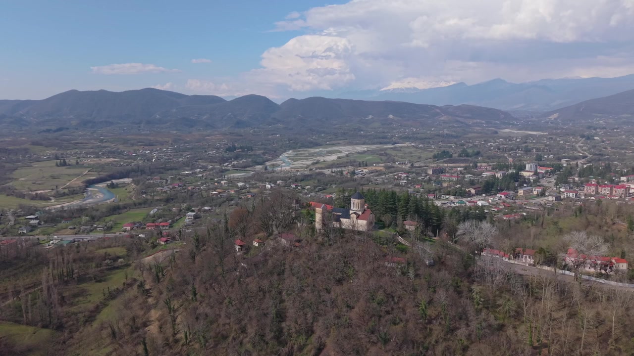 Panoramiczny widok z lotu ptaka na klasztor Martvili, prezentujący jego położenie na wzniesieniu, wijącą się rzekę, zieloną dolinę i malowniczy krajobraz Gruzji.