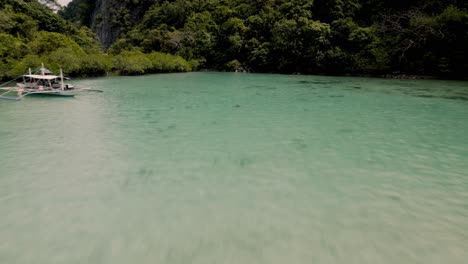 Aerial-drone-shot-close-to-transparent-water-seeing-corals-and-relaxing-on-a-boat-surrounded-by-mountains,-cliffs,-trees,-ocean,-sand,-fishes-while-Island-Hopping-in-Coron-Palawan-in-The-Philippines