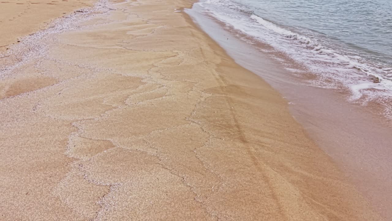 Blødt sand møder blide bølger ved en kystlinje om eftermiddagen