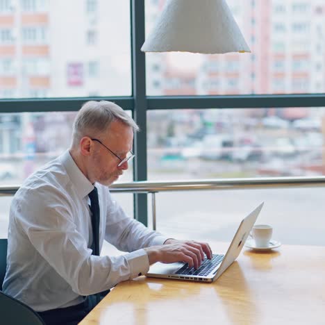 side view of a senior man typing on a laptop. successful businessman in white shirt and tie sitting at the desk and working near the window.