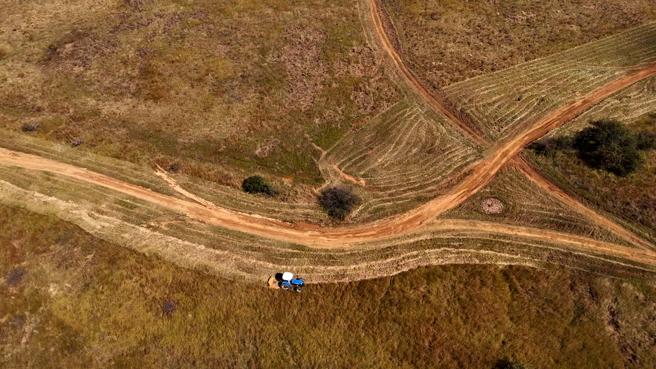 Tractor slashing thick grass next to dirt road before firebreak burn, aerial