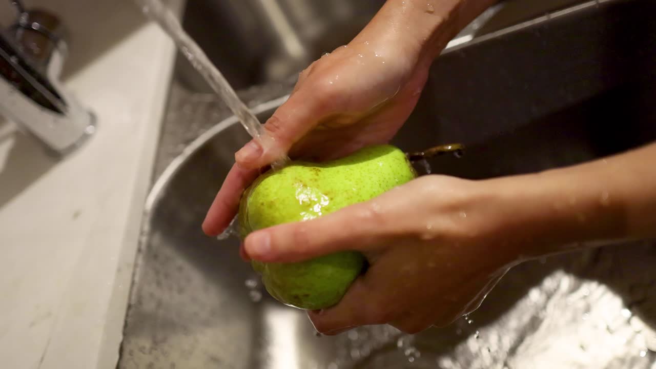 Manos lavando una pera bajo agua corriente