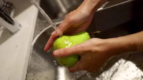 manos lavando una pera bajo agua corriente