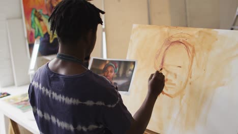 african american male painter painting from photograph on canvas in artist studio