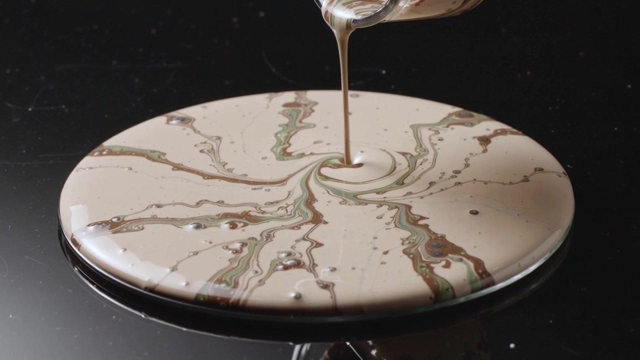 Pouring clear jug contacting center, forming swirl in glass dish on tabletop, creating marbling