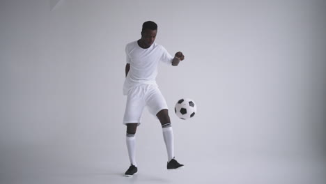 Un-Jugador-De-Fútbol-Negro-Profesional-Con-Uniforme-Blanco-Sobre-Fondo-Blanco-Hace-Malabarismos-Con-Una-Pelota-En-Cámara-Lenta.-Jugador-De-Fútbol-De-Grupo-étnico-Afroamericano-Con-Un-Balón-De-Fútbol