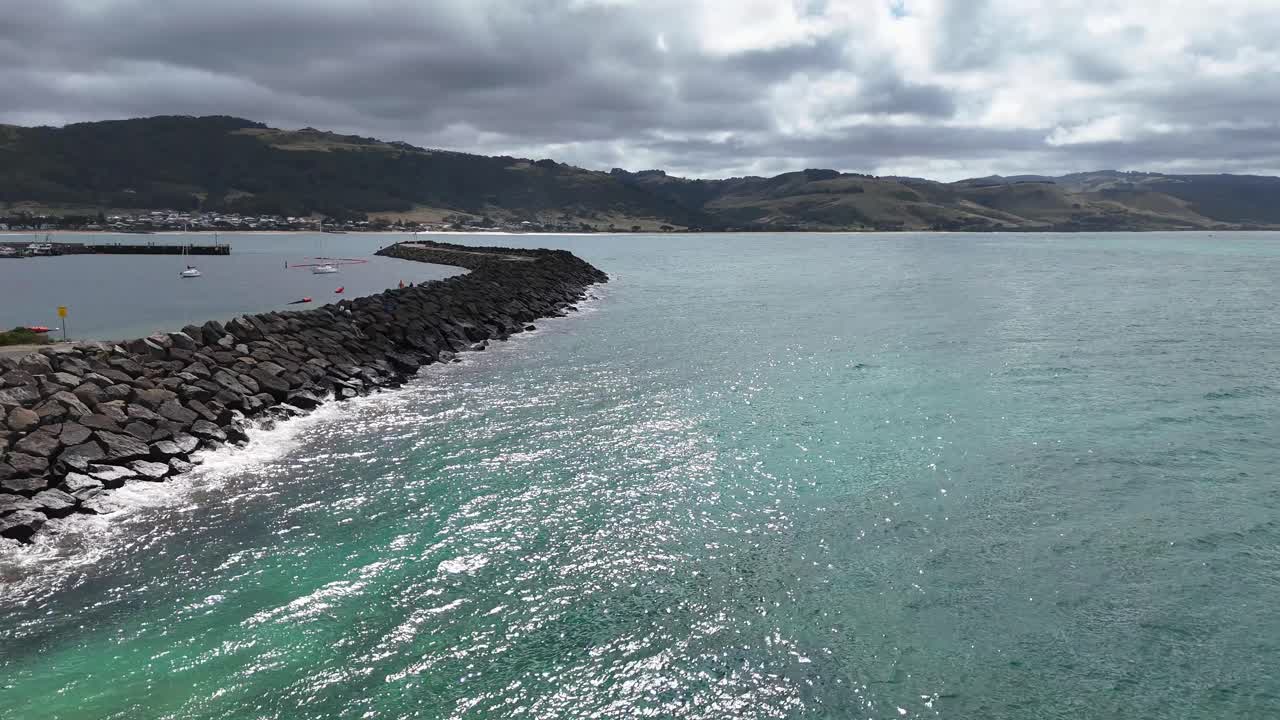 Aerial view of Port Campbell's harbor entrance with turquoise waters and rocky breakwaters under cloudy skies