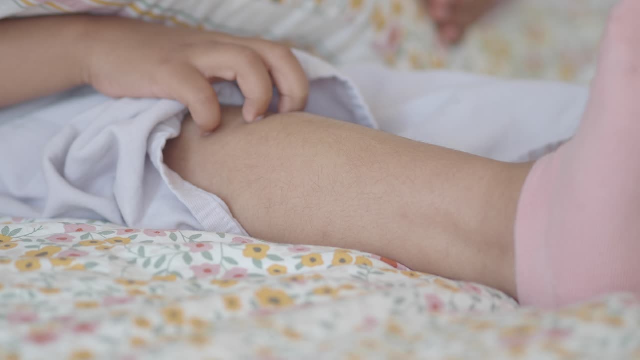 A close-up of a person's leg and hand on a floral bedspread