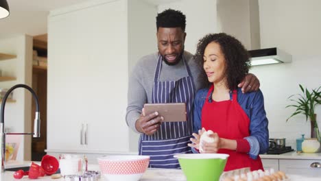 feliz pareja afroamericana usando delantales, usando tableta y horneando juntos