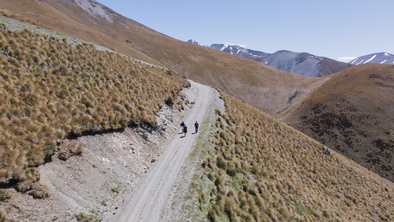 vista aérea rastreando a tres excursionistas por un sinuoso camino de tierra en los alpes de nueva zelanda en un soleado día de primavera