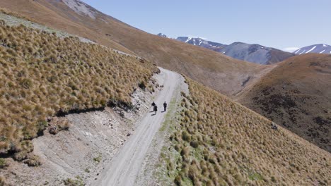 aerial view tracking three hikers up a winding dirt road in the alps of new zealand on a sunny spring day