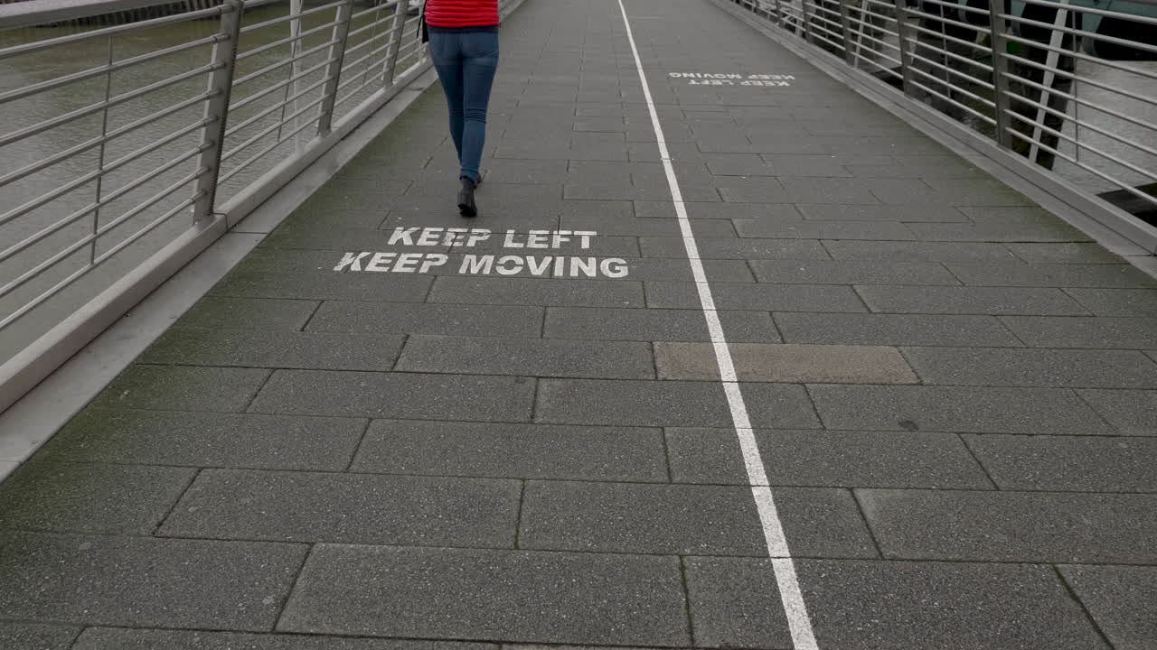 겨울 옷을 입은 독신 여성이 경고 표시를 따라 천천히 황금 희년 다리를 건너고 있습니다.