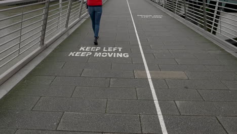 Single-female-in-winter-clothing-slowly-crosses-the-Golden-Jubilee-Bridge,-following-the-warning-markings