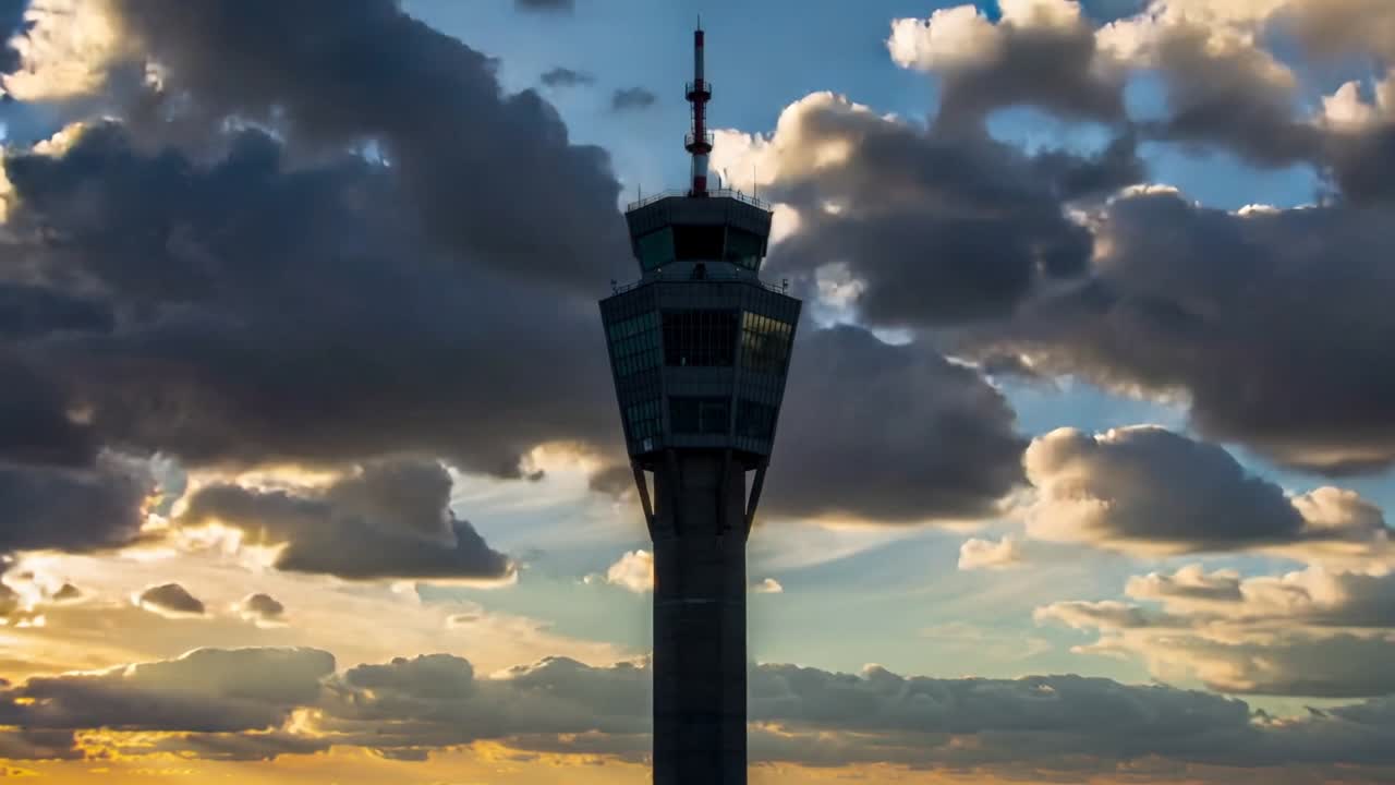 Torre di controllo dell'aeroporto con cabina in vetro e antenna, con il cielo che si schiarisce mentre il sole tramonta.