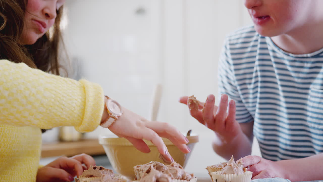 다운 증후군 커플이 집에서 주방에서 아이싱으로 집에서 만든 컵케이크를 장식하고 있습니다.