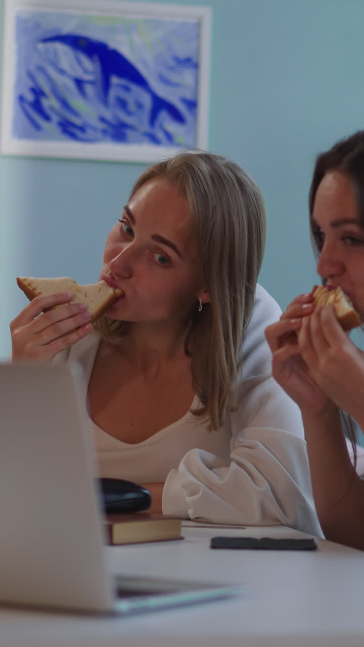 amigas disfrutan de sándwiches frescos viendo películas dramáticas en la computadora portátil. mujer rubia discute el momento con su amiga discapacitada sentada en la mesa de primer plano