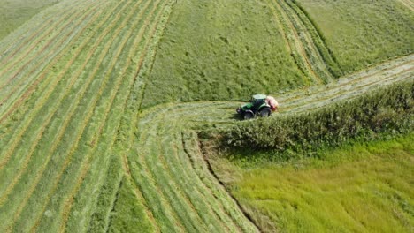 tractor cutting grass of steep green hill field in azores, aerial view