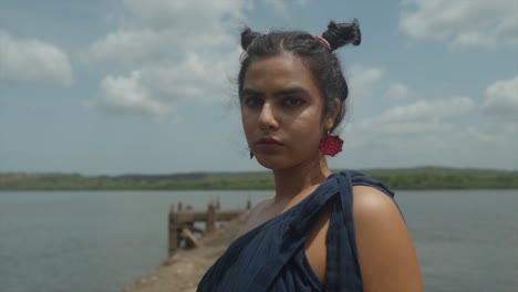 close up of an indian fashion model posing close to the water in a blue red and orange sustainable fasion dress in slow motion