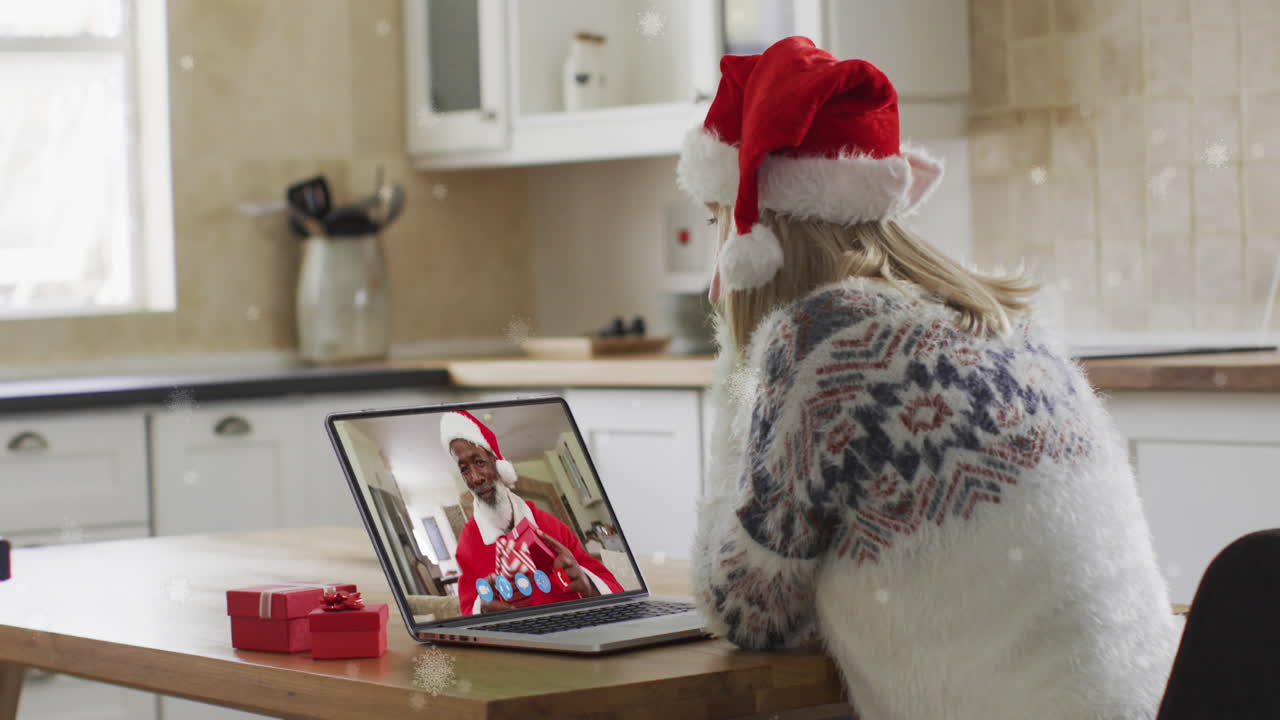 animación de nieve cayendo sobre feliz mujer caucásica en sombrero de santa en llamada de video portátil