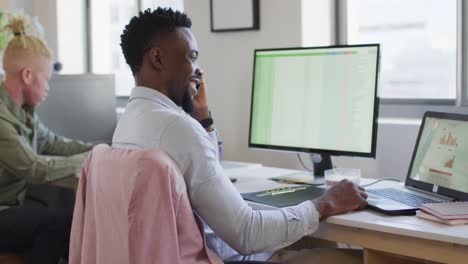 Happy-african-american-businessman-talking-on-smartphone-in-creative-office