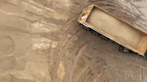 an aerial view of an excavator's bucket lifting sand, creating a cloud of dust against a backdrop of sand dunes