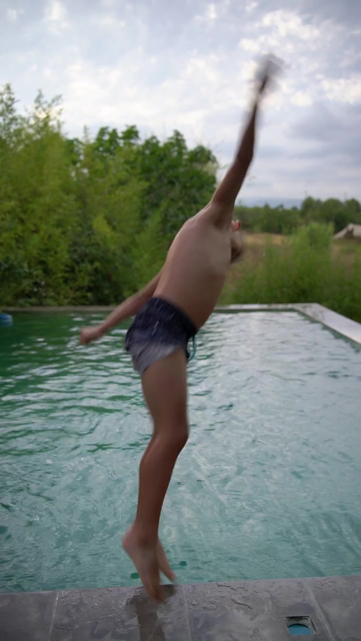 Un bambino di sette anni in posa giocosa sul bordo di una piscina a sfioro, prima di tuffarsi in acqua, Verticale.
