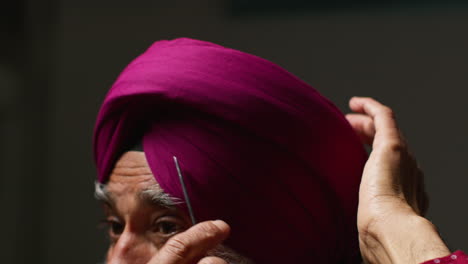 close up low key studio lighting shot of senior sikh man with beard using salai needle when putting on turban against dark background