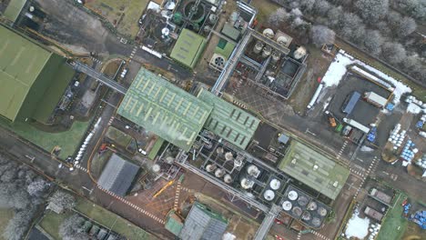 winter overhead drone aerial footage of a large industrial plant showing pipework structures, buildings, cooling towers, steam, and work vehicles