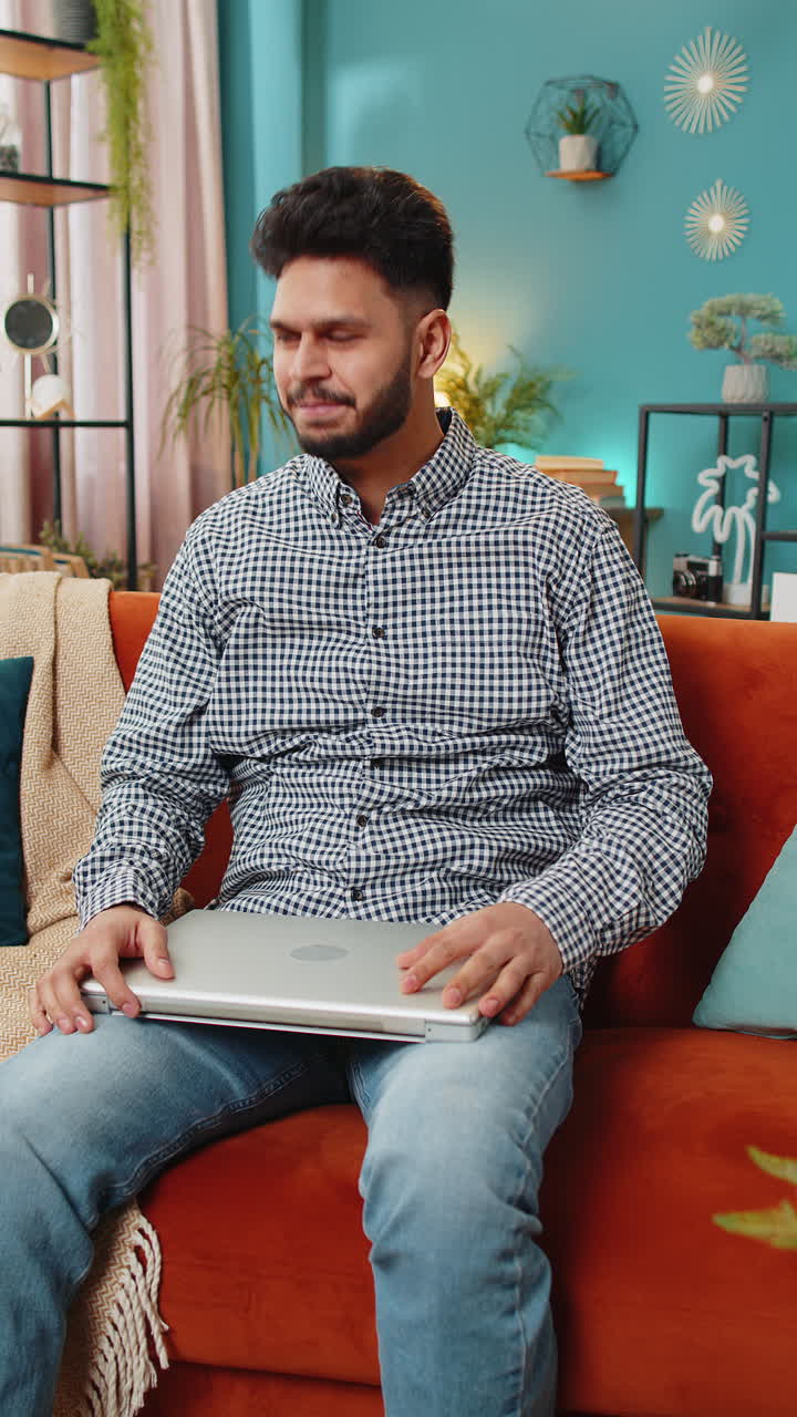 joven independiente sentado en el sofá cerca de la computadora portátil después de terminar el trabajo en la sala de estar en casa