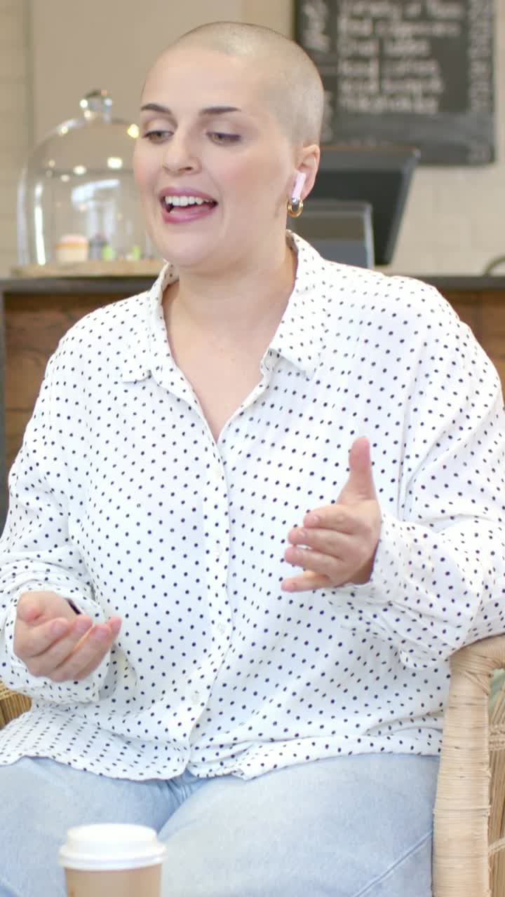 Video verticale: Donna con camicia a pois che parla e risponde a una domanda in un caffè, gesticolando verso una tazza e un portatile.