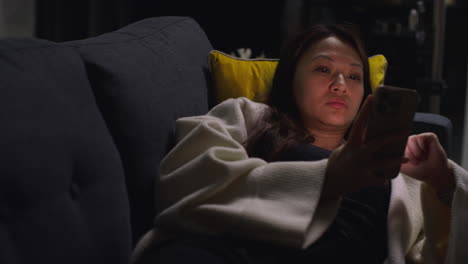 close up of woman spending evening at home lying on sofa with mobile phone scrolling through internet or social media 6