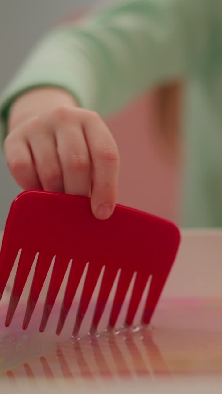 Girl uses comb to draw on oily water surface in tray at table in classroom closeup slow motion. Traditional Ebru design lesson for junior students