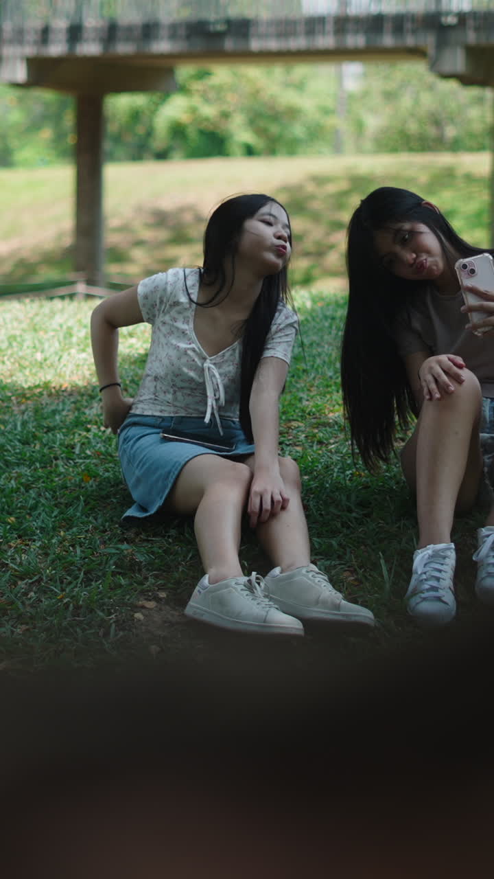 หญิงสาวชาวเอเชียสองคนถ่ายเซลฟี่และโพสท่าในสวนสาธารณะ