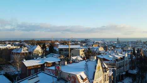 aerial slow take off revealing snow-covered old buildings rooftops of sopot city on baltic sea background at sunset