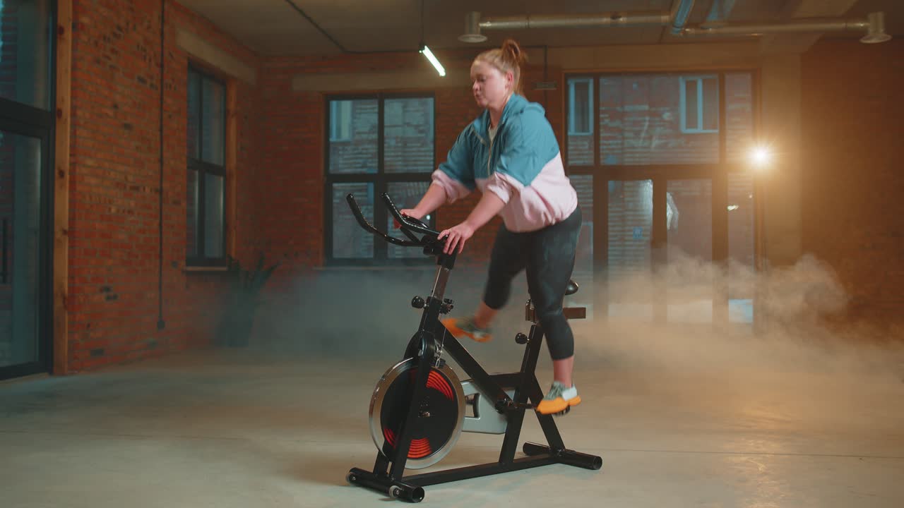 Athletic woman riding on spinning stationary bike training routine in haze gym weight loss indoors