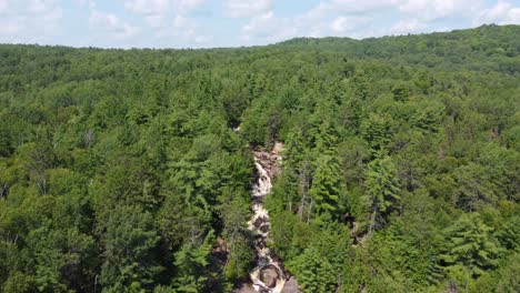 Duchesnay-Falls-peeks-from-thick-green-forest-canopy-ontario-canada,-aerial-descend