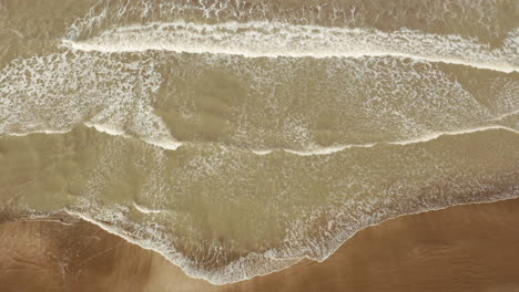 aerial view of small sea waves advancing towards the golden sandy coast at sunset