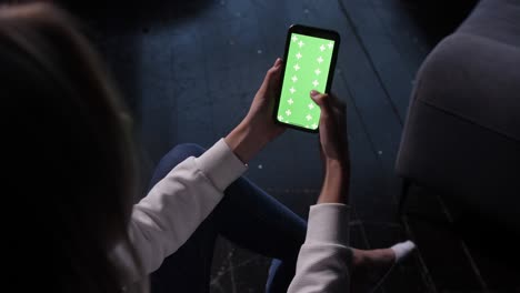 la señora se sienta en el sofá con el teléfono inteligente en las manos. pantalla verde chromakey mock up.