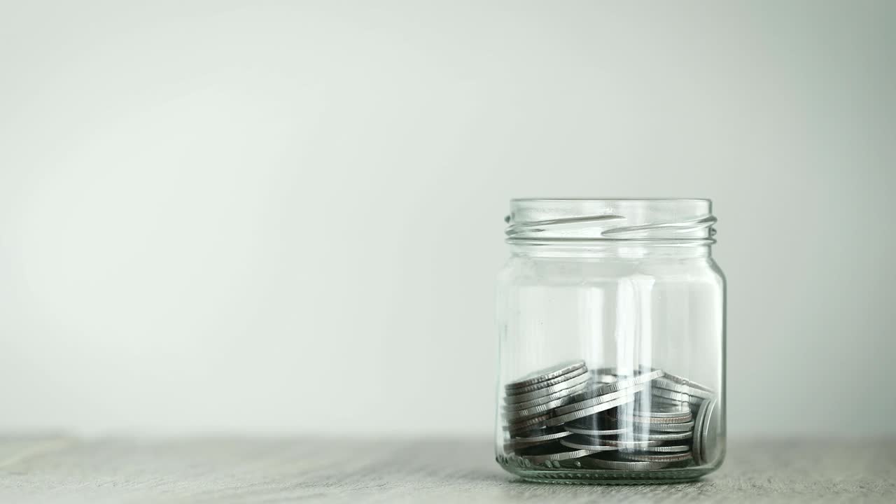 Close up Money coin falling into glass jar , a money saving , donation or business financial growth concept , 4K Dci resolution , vintage retro color tone