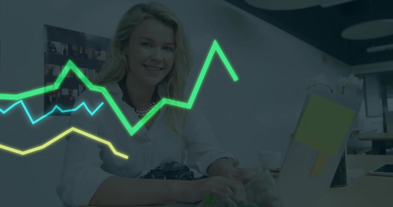 Donna adulta seduta alla scrivania, con sovrapposizioni di grafici verde neon in uno spazio di lavoro tecnologico aziendale.
