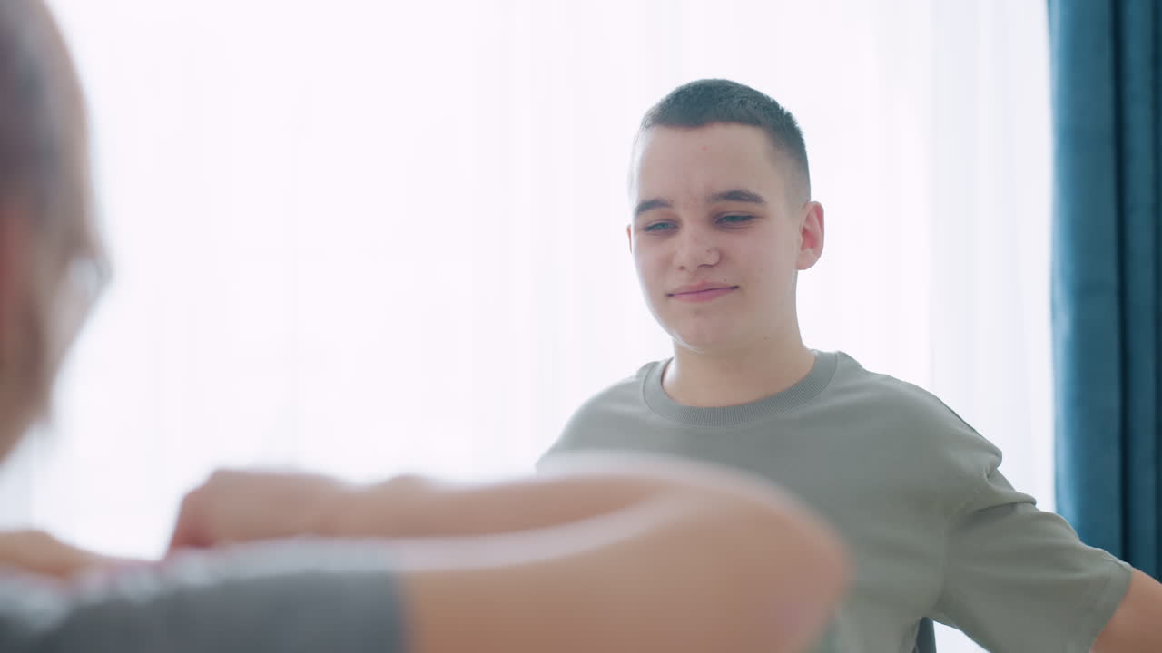 밝은 방에서 커튼 배경을 두고 실내 피트니스 트레이닝을 하는 동안 차분한 미소를 지으며 운동 세션을 즐기는 자신감과 웰빙을 보여주는 소년