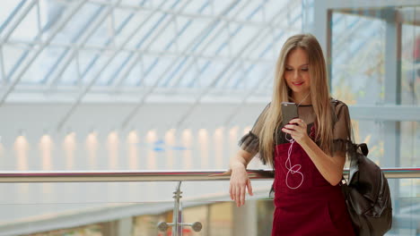 Una-Joven-Turista-Con-Sombrero,-Con-Mochila-Se-Encuentra-En-El-Aeropuerto-Y-Usa-Un-Teléfono-Inteligente.-Una-Chica-Hipster-Revisa-El-Correo-Electrónico,-Chatea,-Escribe-Blogs,-Navega-Por-Internet.-Marketing-En-Línea,-Educación.-Trabajo-A-Distancia,-E-learning.