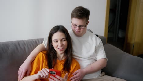 hombre con síndrome de down sentado en el sofá con una chica, ella está usando el teléfono móvil, la pantalla de desplazamiento