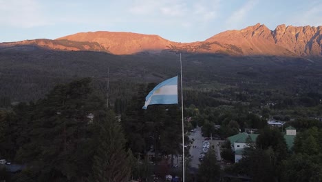 argentinian flag waving over town and in the background a sunlit mountain of land