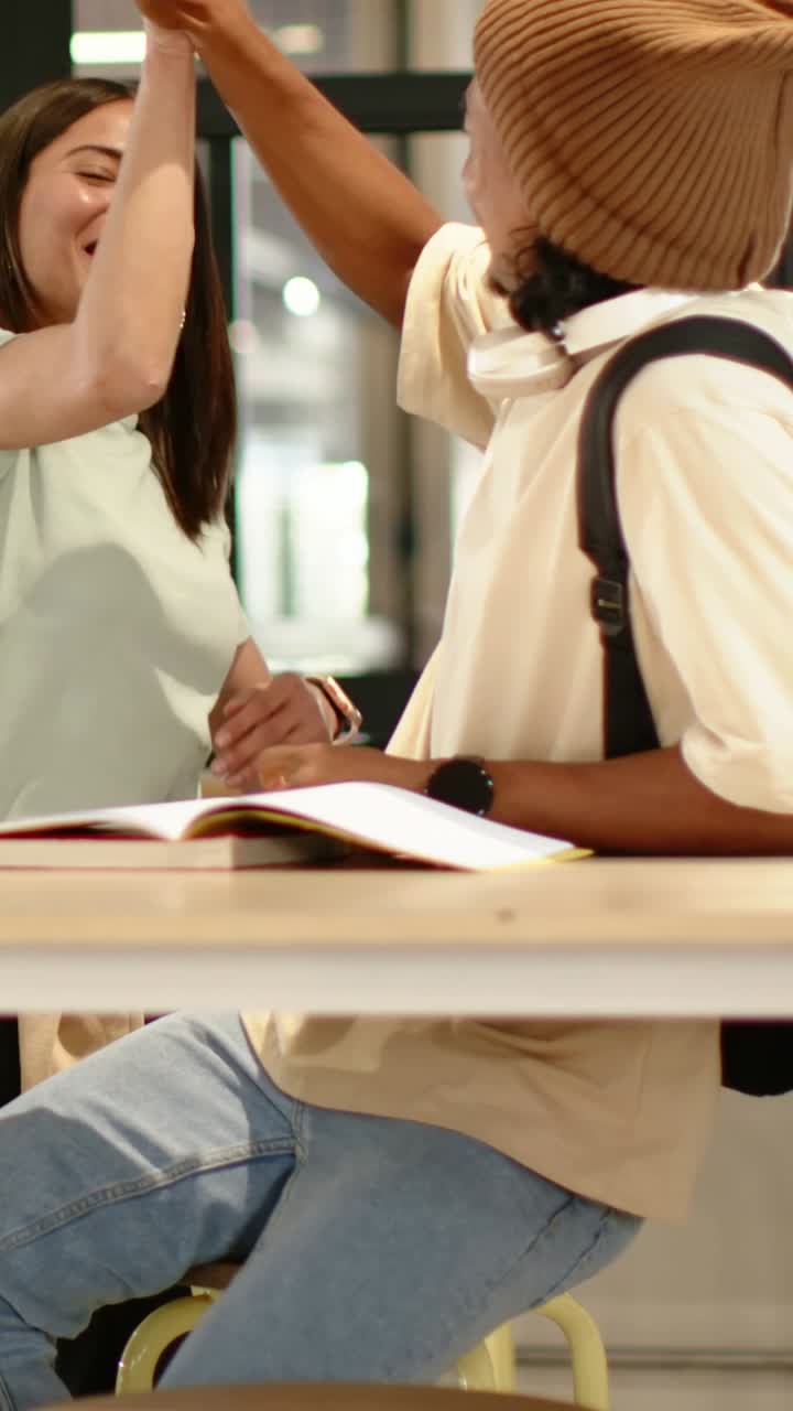 Vertical video: Talking students celebrating high-five at study table, then returning to open book