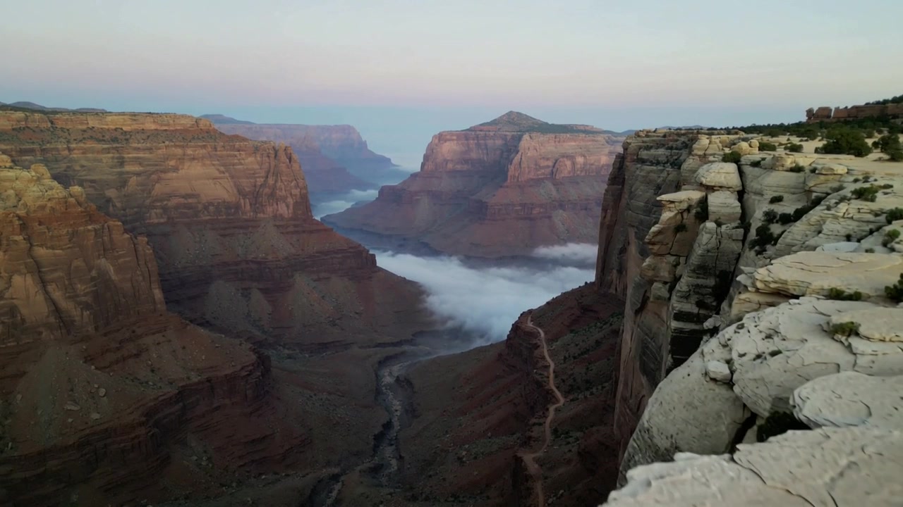 Shifting fog filling canyon at overlook as dawn light warming sandstone cliffs and revealing ledge