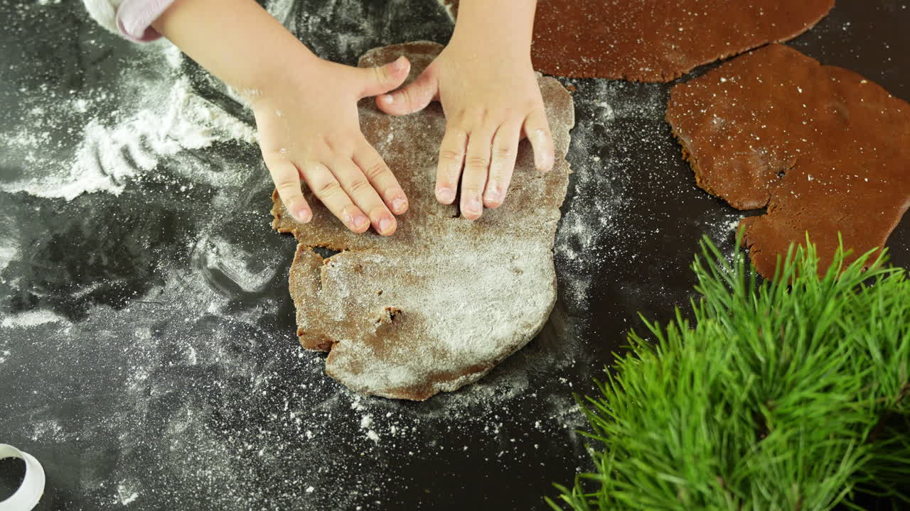 Hands of a child moulding Christmas gingerbread dough on black table - view from above, Close-up, covered with a bit of flour